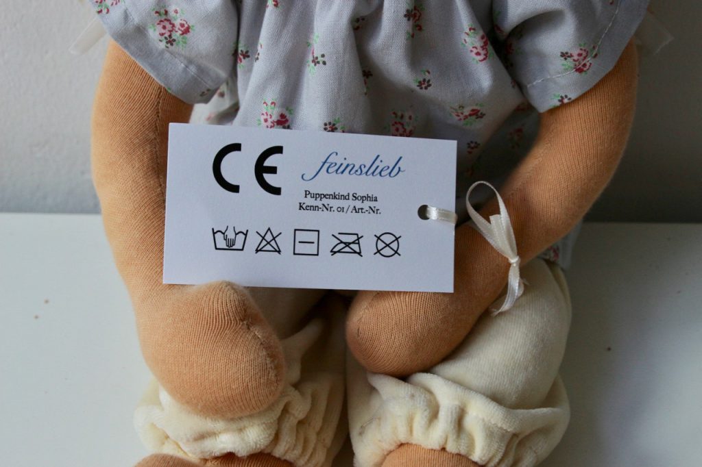 Oberkörper einer Puppe, die am Arm ein Etikett mit CE-Kennzeichnung und Wäschesymbolen hat 