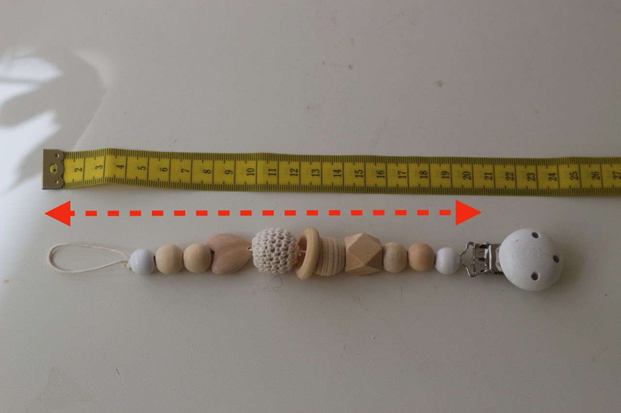 Schnullerkette Länge messen: Welchen Abstand man misst, dargestellt mit Lineal, Schnullerkette und Abstandspfeil